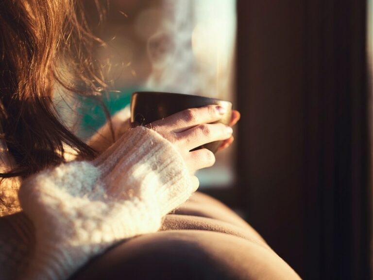 Destaque para mãos femininas segurando uma xícara de café fumegando