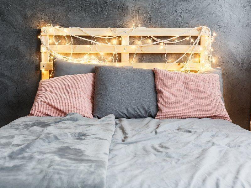 Imagem de um quarto de casal com cabeceira de luzes natalinas