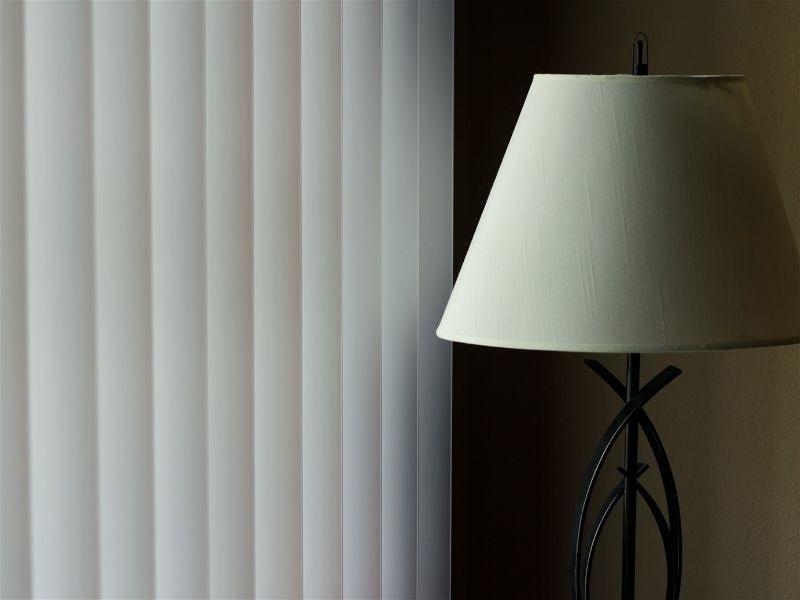 Imagem em destaque de um abajur com tripé ao lado de uma cortina 