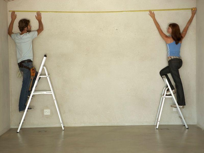 Imagem de casal medindo parede com fita métrica