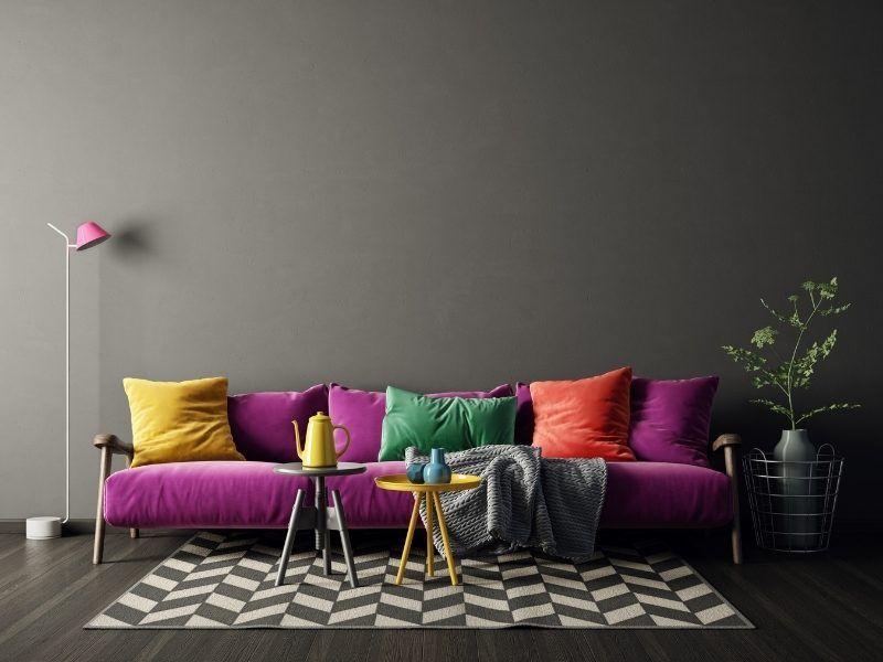 Sala de estar com sofá roxo e almofadas nas cores amarelo, verde e vermelho 