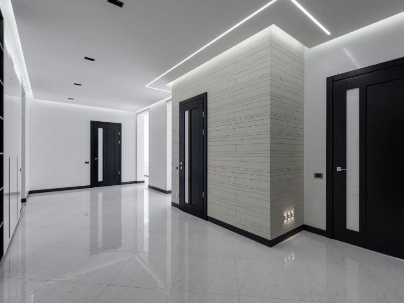 ambiente corporativo com pisos, paredes claras, portas pretas e iluminação fria