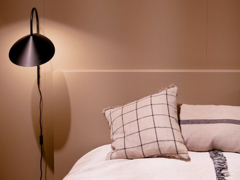 luminária acessa ao lado de uma cama arrumada com colchas brancas