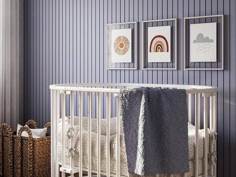 quarto de um bebê com berço, cesto e quadros aplicados em um painel ripado azul