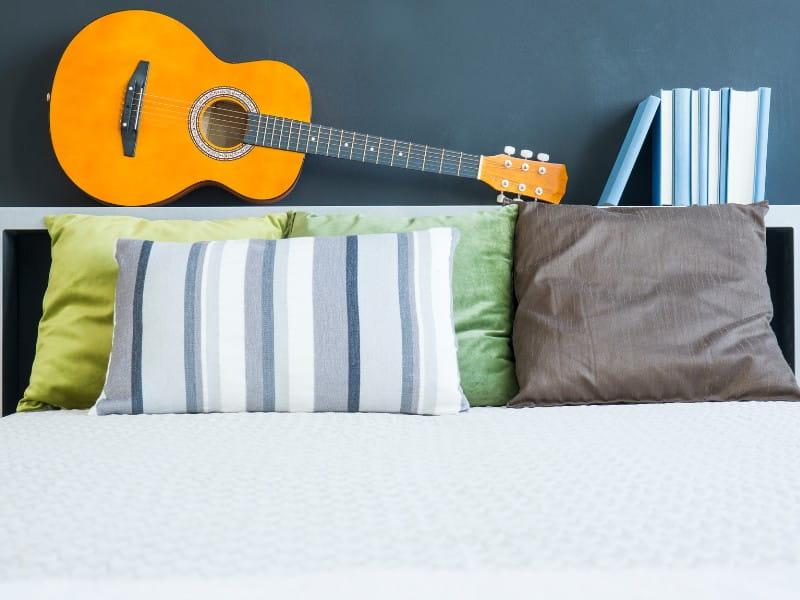 cama com cabeceira multificional que está apoiando violão e livros
